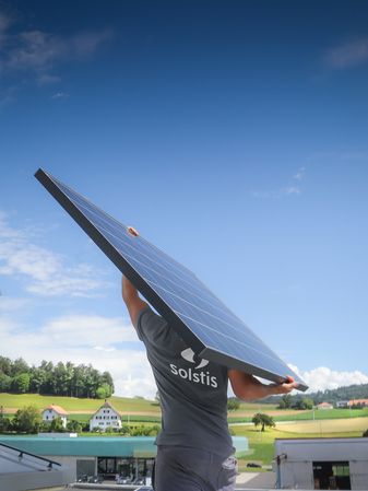 Ein Solstis-Installateur trägt ein Photovoltaikmodul auf einer Baustelle